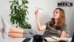 Woman sitting with feet on desk and paper airplane in hand procrastinating.